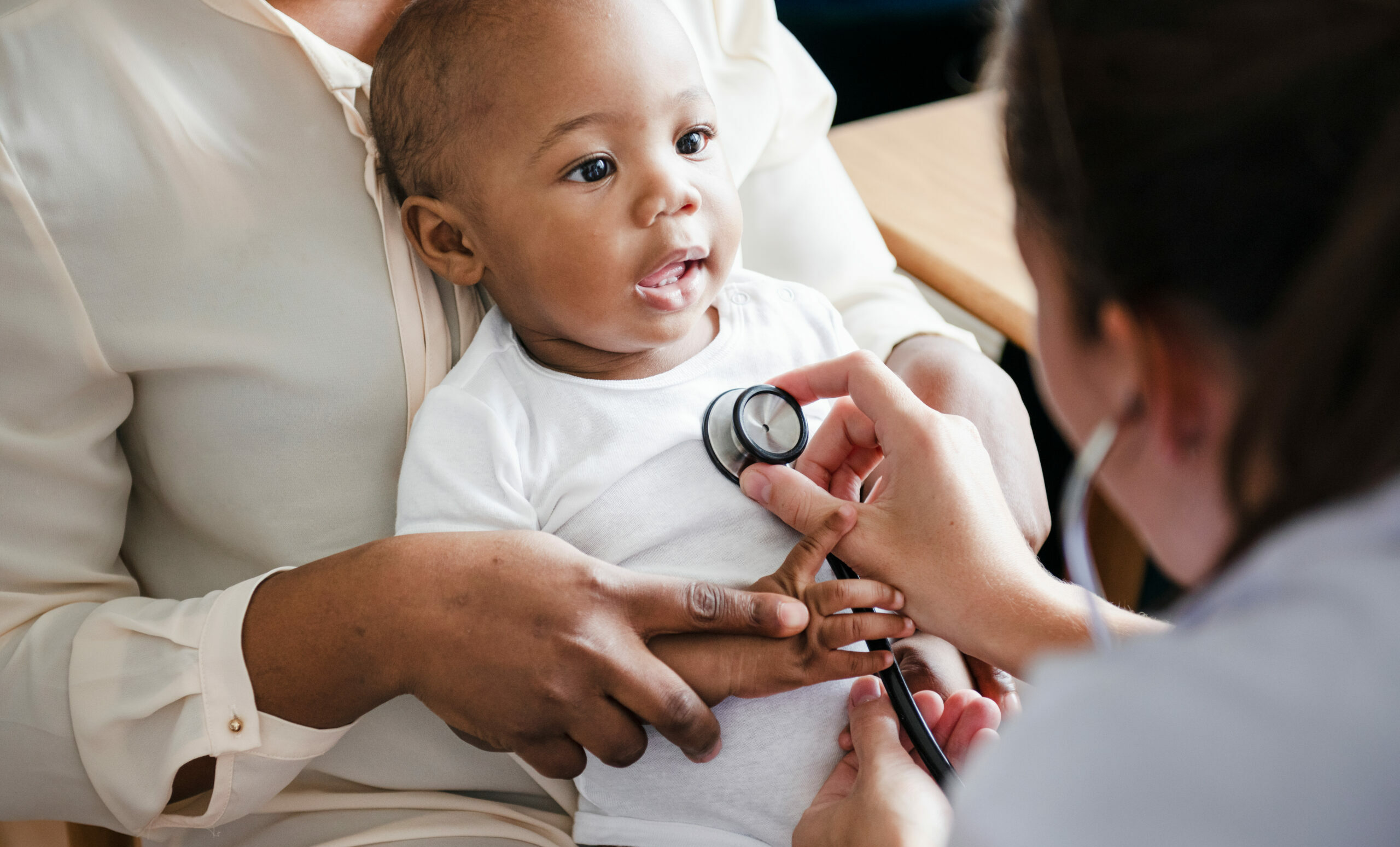 Photo d'une médecin pédiatre en train d'examiner une enfant assise sur les genoux de son parent